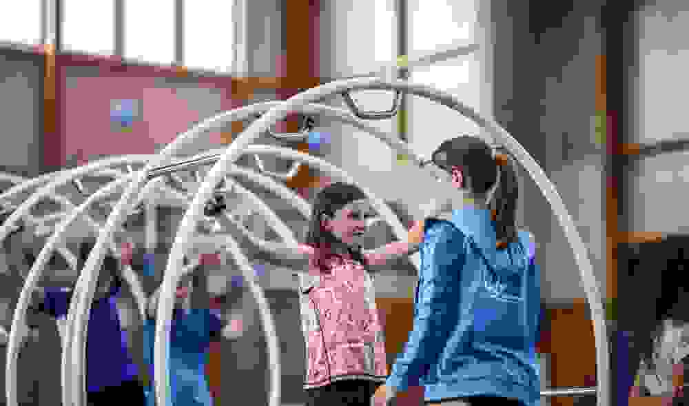 Ein Mädchen instruiert ein jüngeres Mädchen, das in einem Rhönrad steht.